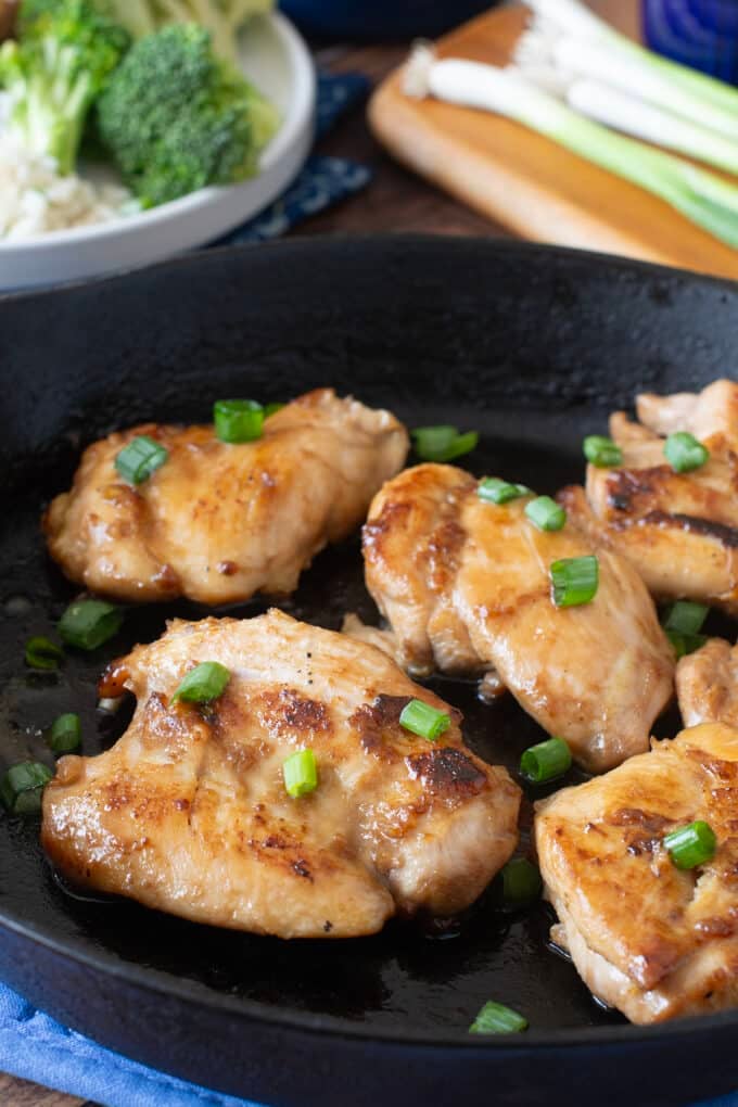 Teriyaki chicken thighs in a cast iron pan topped with green onion.