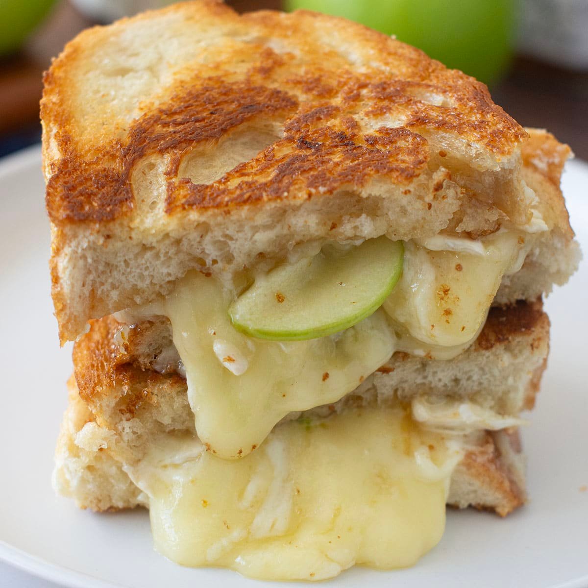 Grilled cheese sandwich halves stacked on plate, melty Brie cheese and apple slices showing.