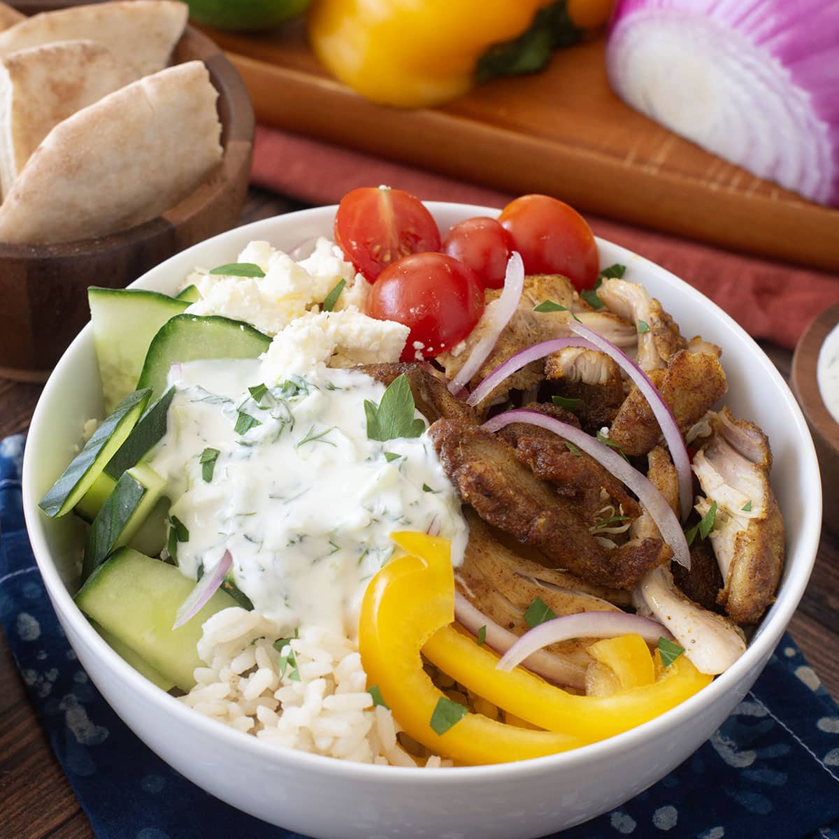 White bowl with shawarma chicken, cherry tomatoes, cucumbers, and more on top of rice.