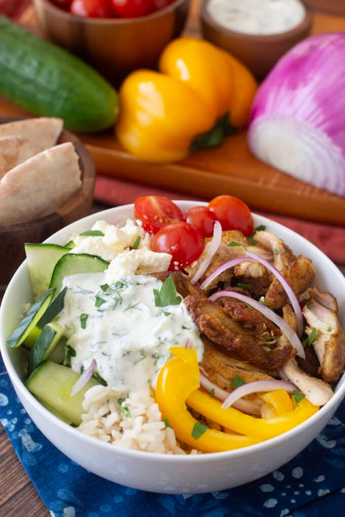 White bowl with shawarma chicken, cherry tomatoes, cucumbers, and more on top of rice.