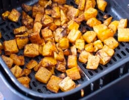 Cubes of browned butternut squash in air fryer basket.