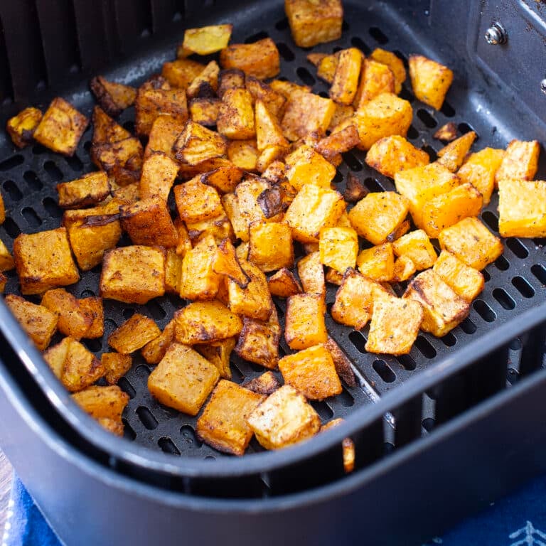 Cubes of browned butternut squash in air fryer basket.