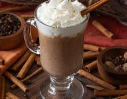 Glass mug with pumpkin hot chocolate topped with whipped cream.