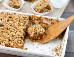 White dish and wooden spatula with pumpkin pie bars with oat topping.