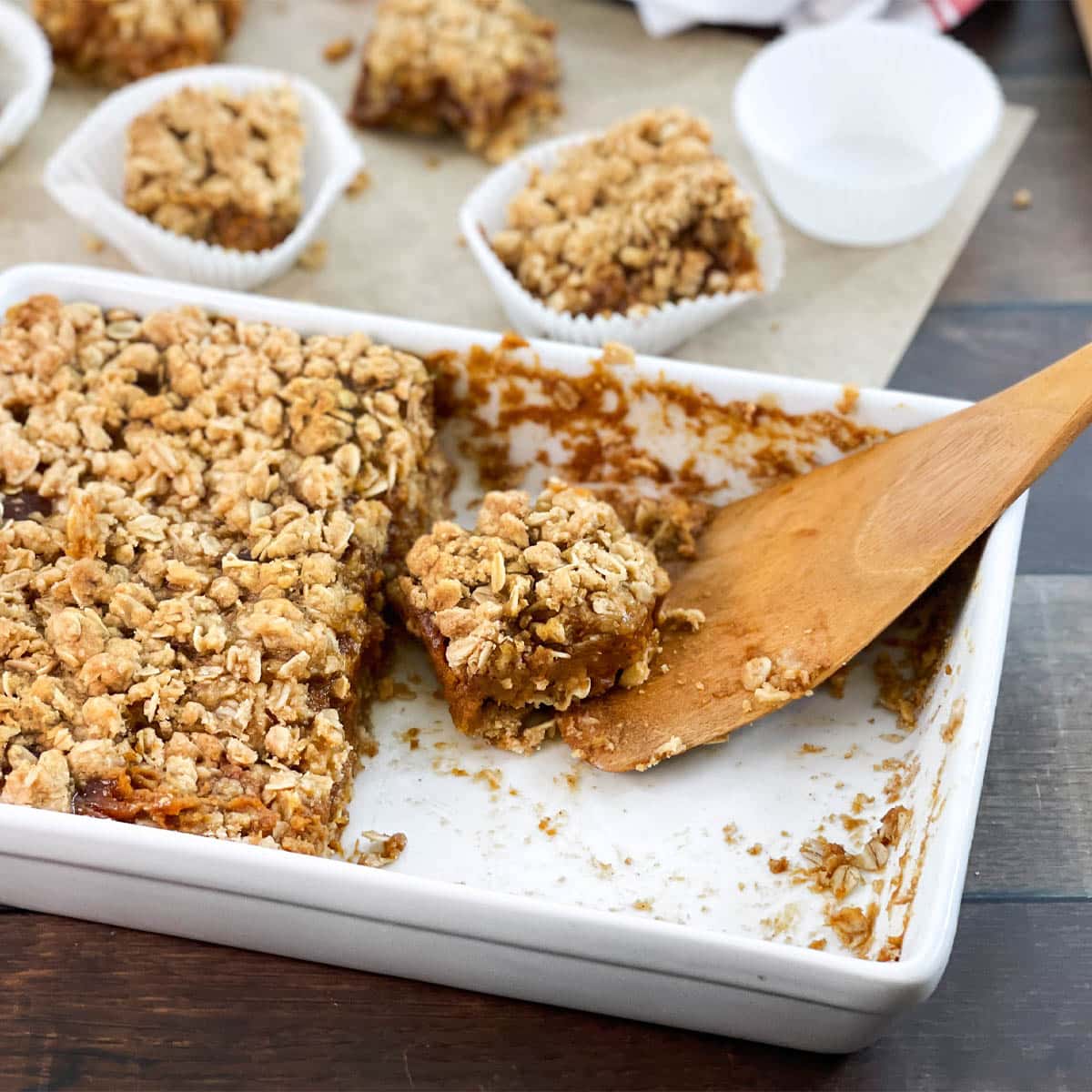 White dish and wooden spatula with pumpkin pie bars with oat topping.