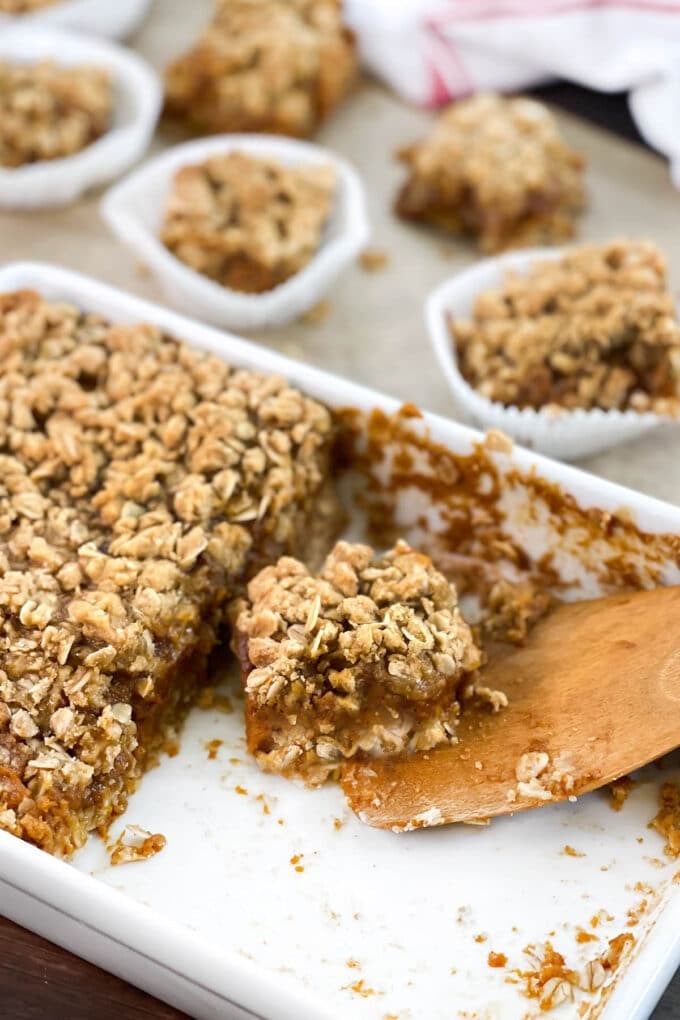 White dish and wooden spatula with pumpkin pie bars with oat topping.