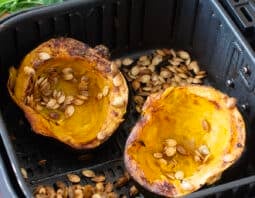 Cooked acorn squash halves and seeds in air fryer basket.