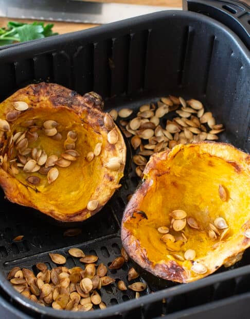 Cooked acorn squash halves and seeds in air fryer basket.