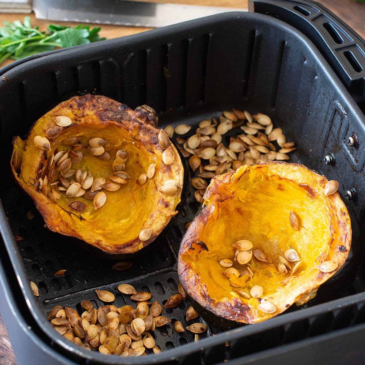 Cooked acorn squash halves and seeds in air fryer basket.