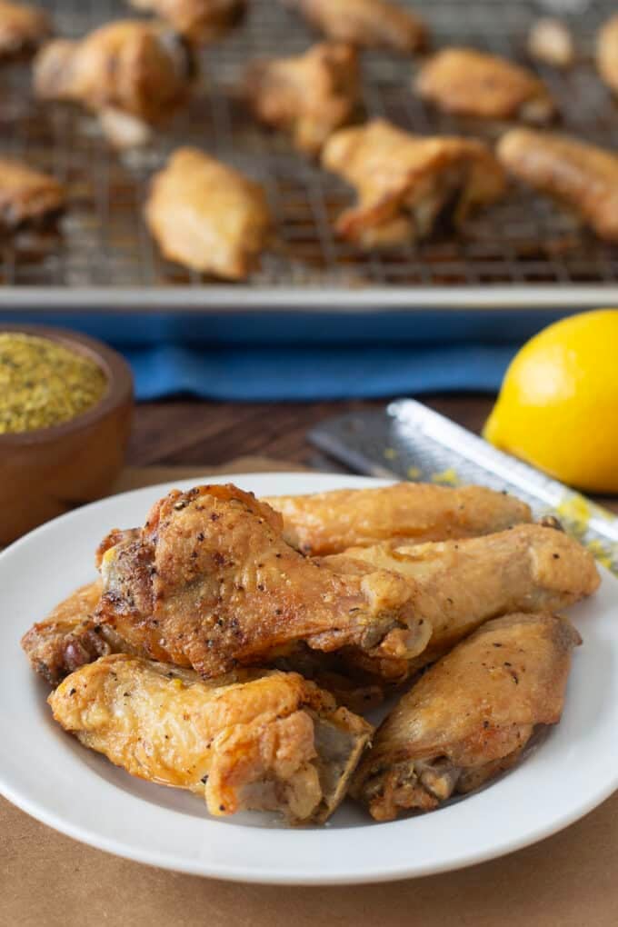 Plate of lemon pepper wings with bowl of seasoning and fresh lemon in back,