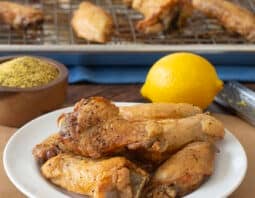 Plate of lemon pepper wings with bowl of seasoning and fresh lemon in back,