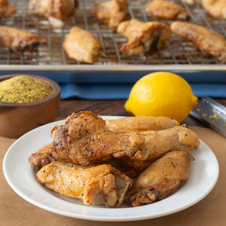 Plate of lemon pepper wings with bowl of seasoning and fresh lemon in back,
