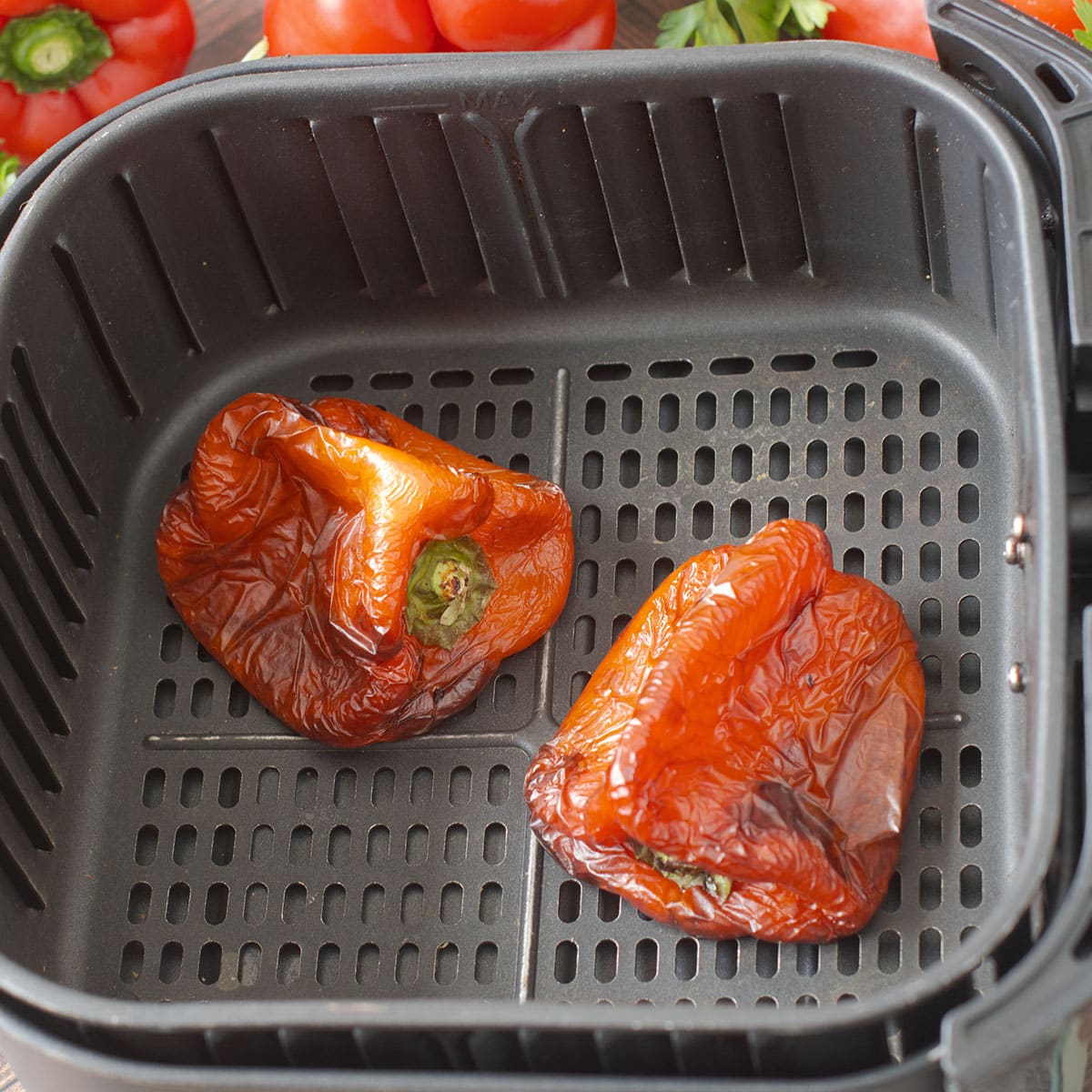 Two whole roasted red peppers in air fryer basket.