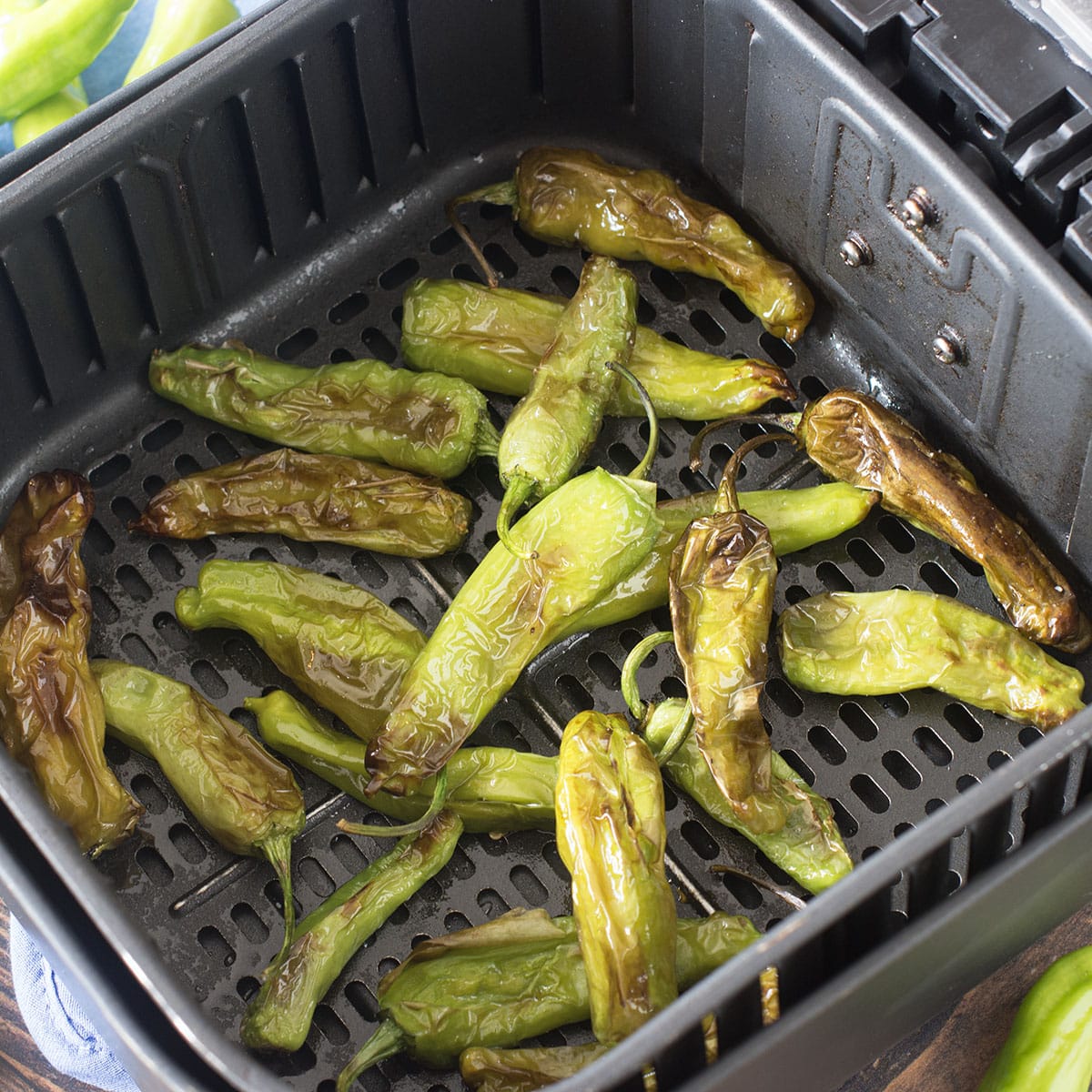 Blistered shishito peppers in the air fryer basket.