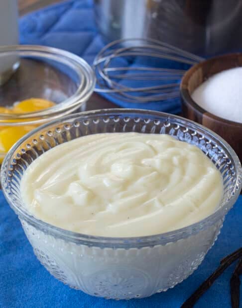 Glass bowl of vanilla custard with eggs and sugar in background.