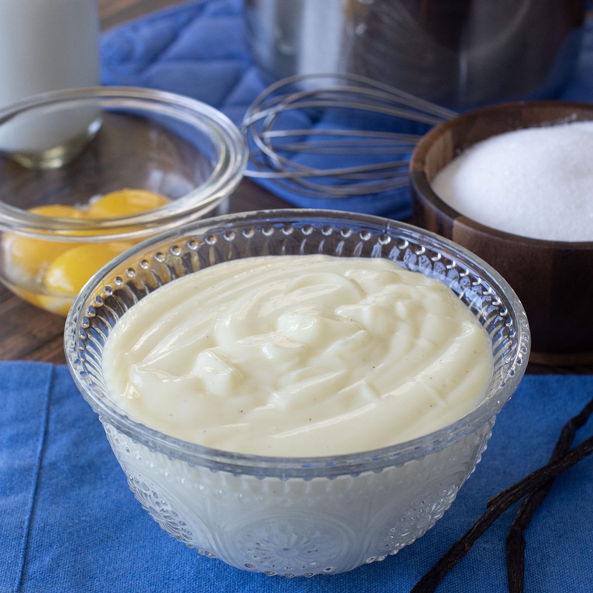 Glass bowl of vanilla custard with eggs and sugar in background.