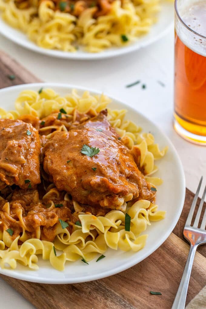 Chicken paprikash over egg noodles on a white plate.