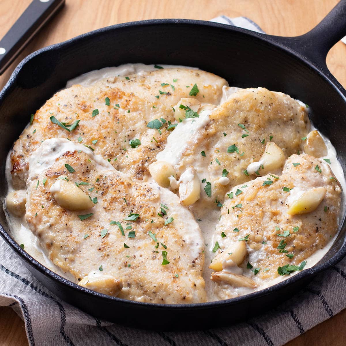 Cast iron skillet with chicken breasts in a creamy garlic sauce with whole garlic cloves.