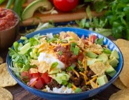 Blue bowl with rice, taco meat, veggies, sour cream, salsa, and more.