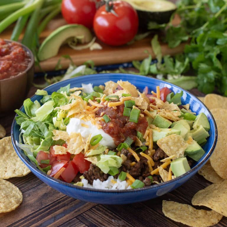 Blue bowl with rice, taco meat, veggies, sour cream, salsa, and more.