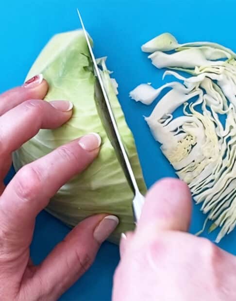 A halved head of cabbage being sliced thinly for coleslaw.
