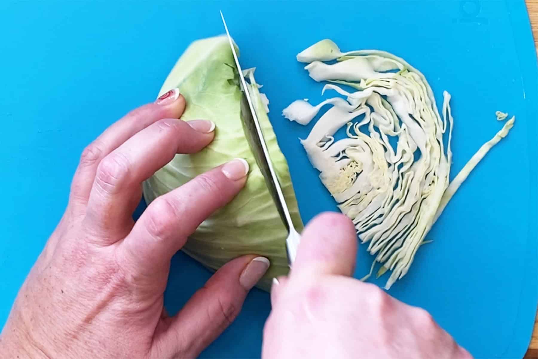 A halved head of cabbage being sliced thinly for coleslaw.