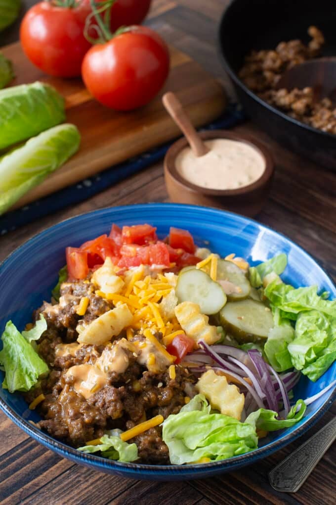 Blue bowl with lettuce, ground beef, cheese, veggies, and french fry croutons.