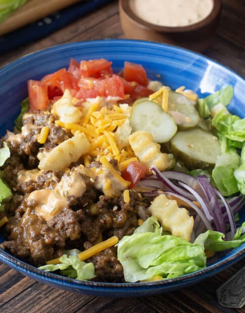 Blue bowl with lettuce, ground beef, cheese, veggies, and french fry croutons.