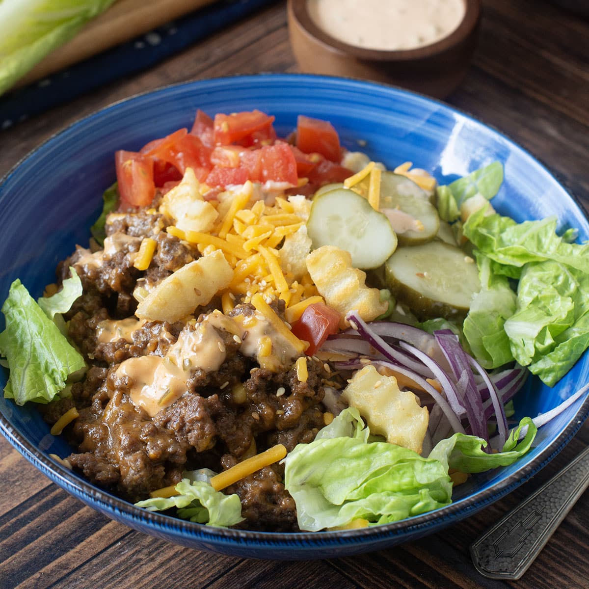 Blue bowl with lettuce, ground beef, cheese, veggies, and french fry croutons.