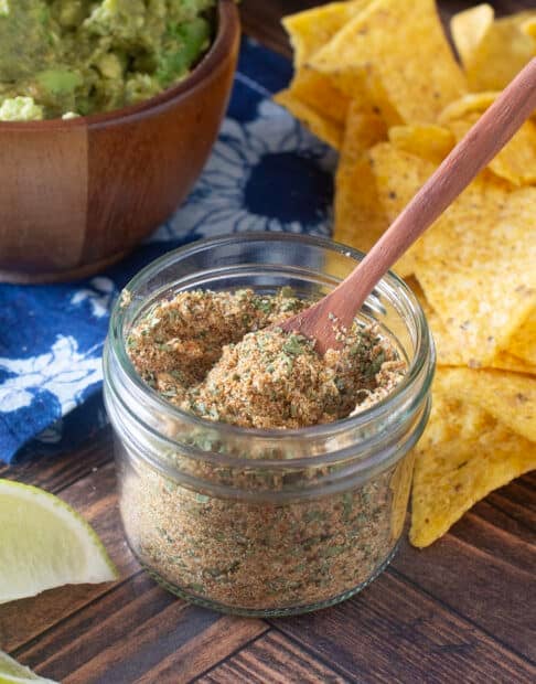 Glass jar with little wooden spoon of guacamole seasoning.