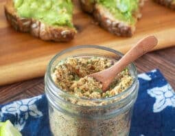 Glass jar with small wood spoon of avocado seasoning mix.