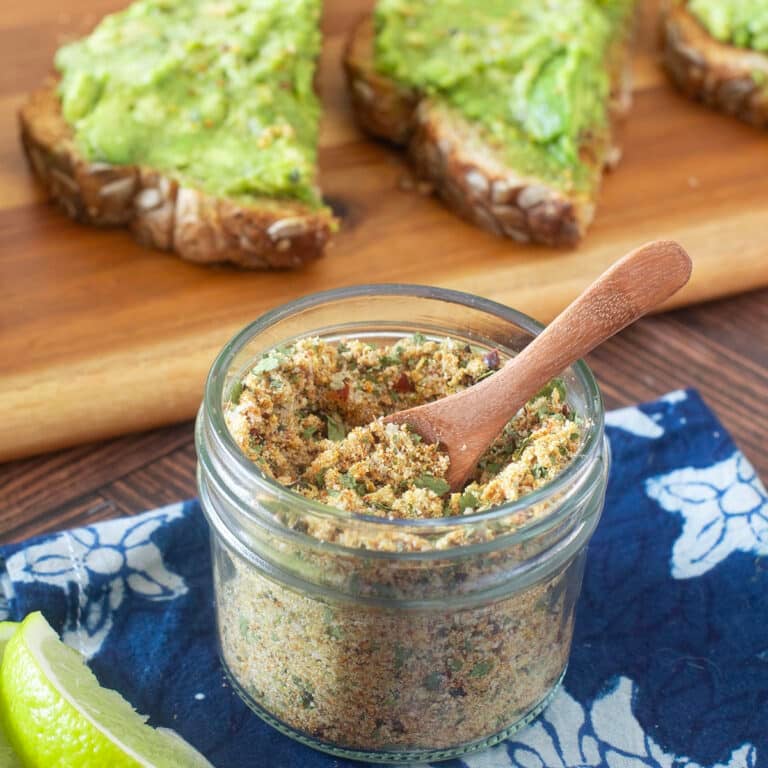 Glass jar with small wood spoon of avocado seasoning mix.