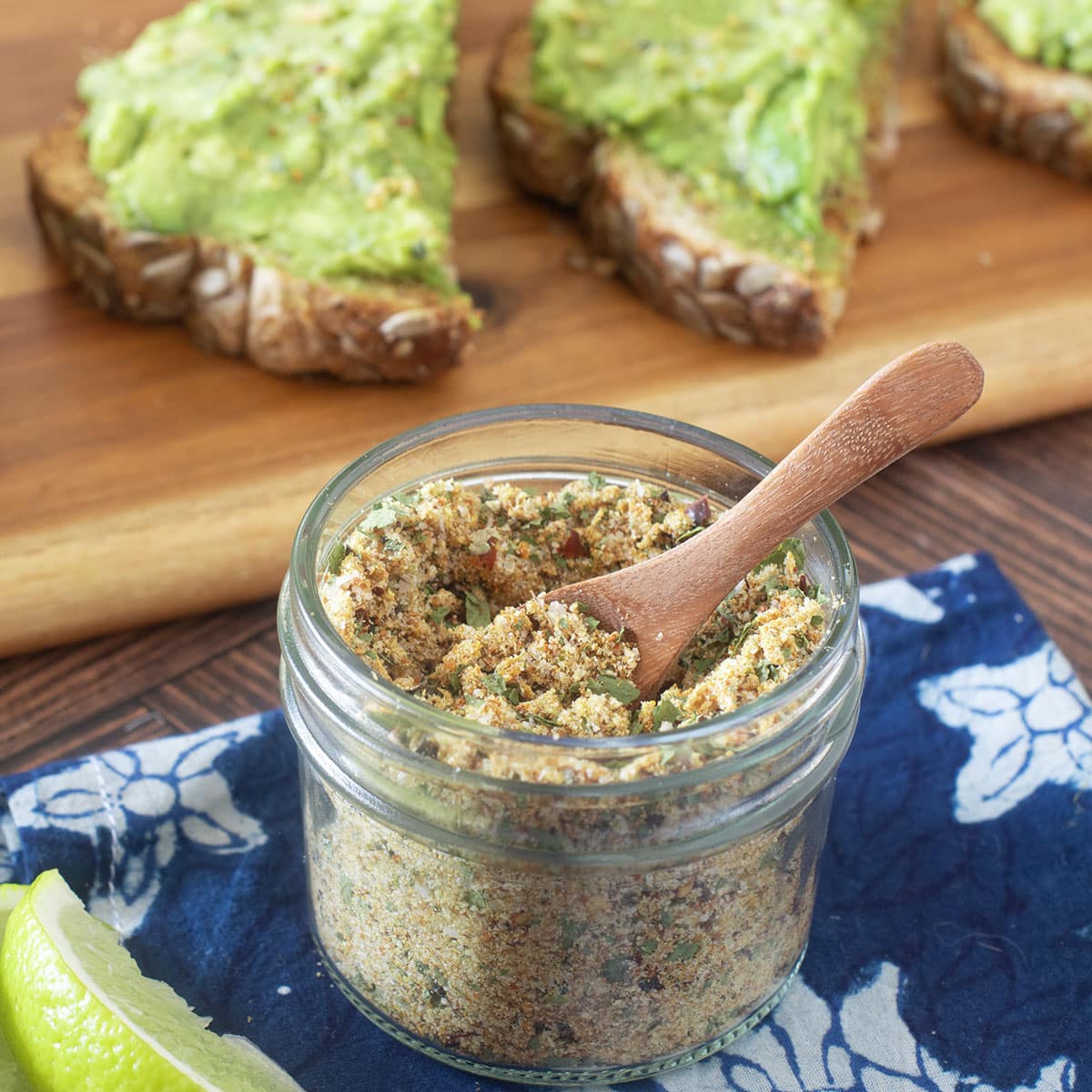 Glass jar with small wood spoon of avocado seasoning mix.