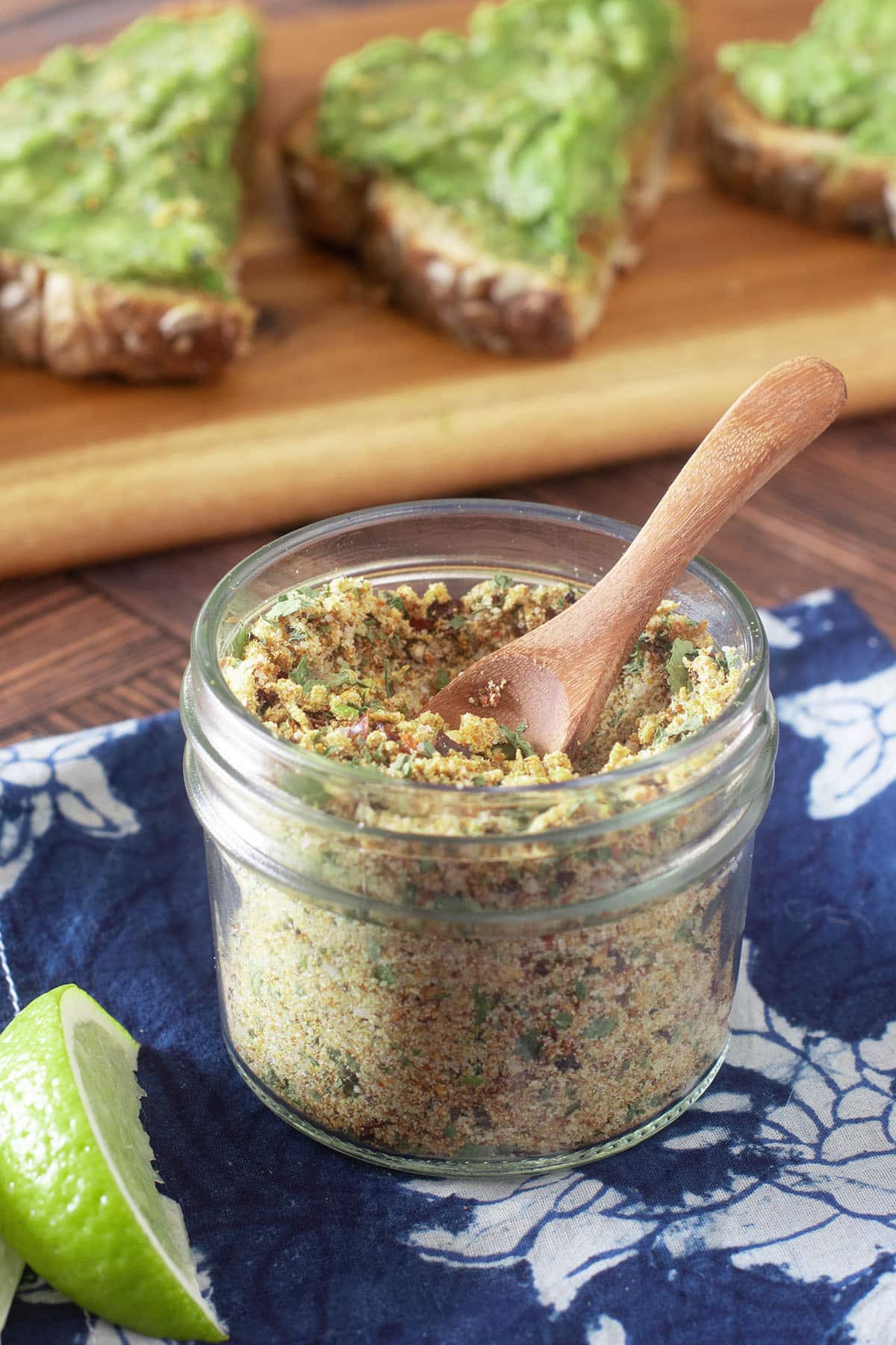 Glass jar with small wood spoon of avocado seasoning mix.