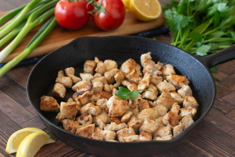 Bite-sized cubes of cooked chicken breast in a cast iron skillet.