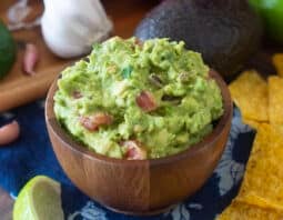 Wooden bowl of homemade guacamole with fresh ingredients around.