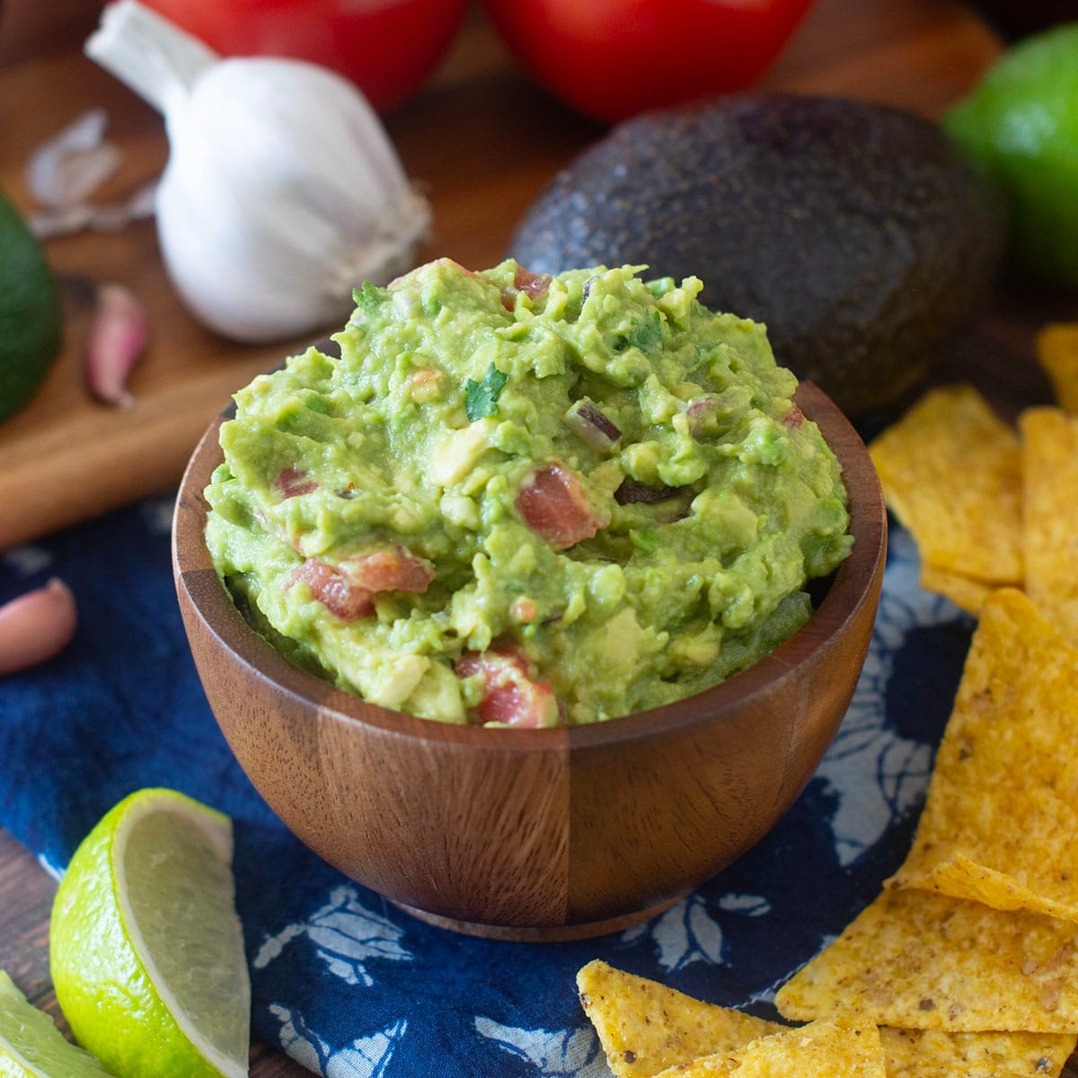 Wooden bowl of homemade guacamole with fresh ingredients around.