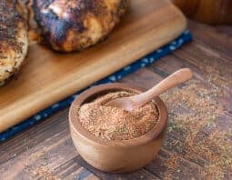 Small wooden bowl of blackened seasoning with blackened chicken behind.