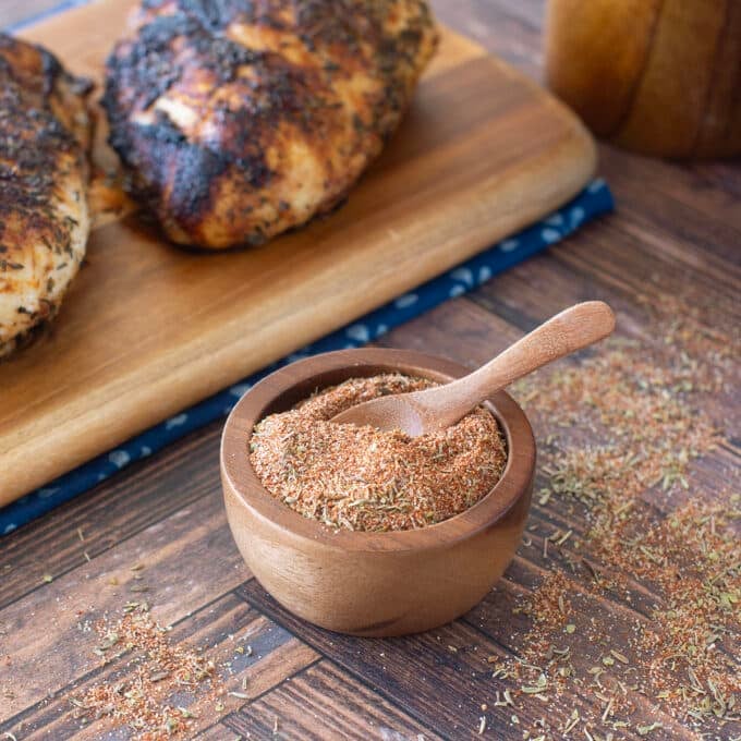 Small wooden bowl of blackened seasoning with blackened chicken behind.