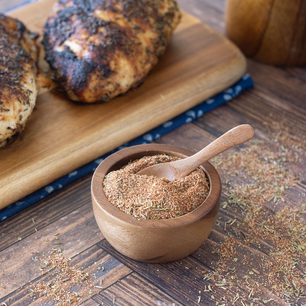 Small wooden bowl of blackened seasoning with blackened chicken behind.