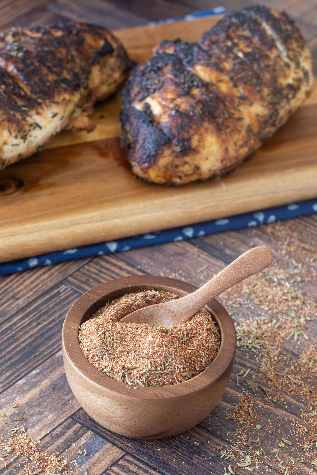 Small wooden bowl of blackened seasoning with blackened chicken behind.