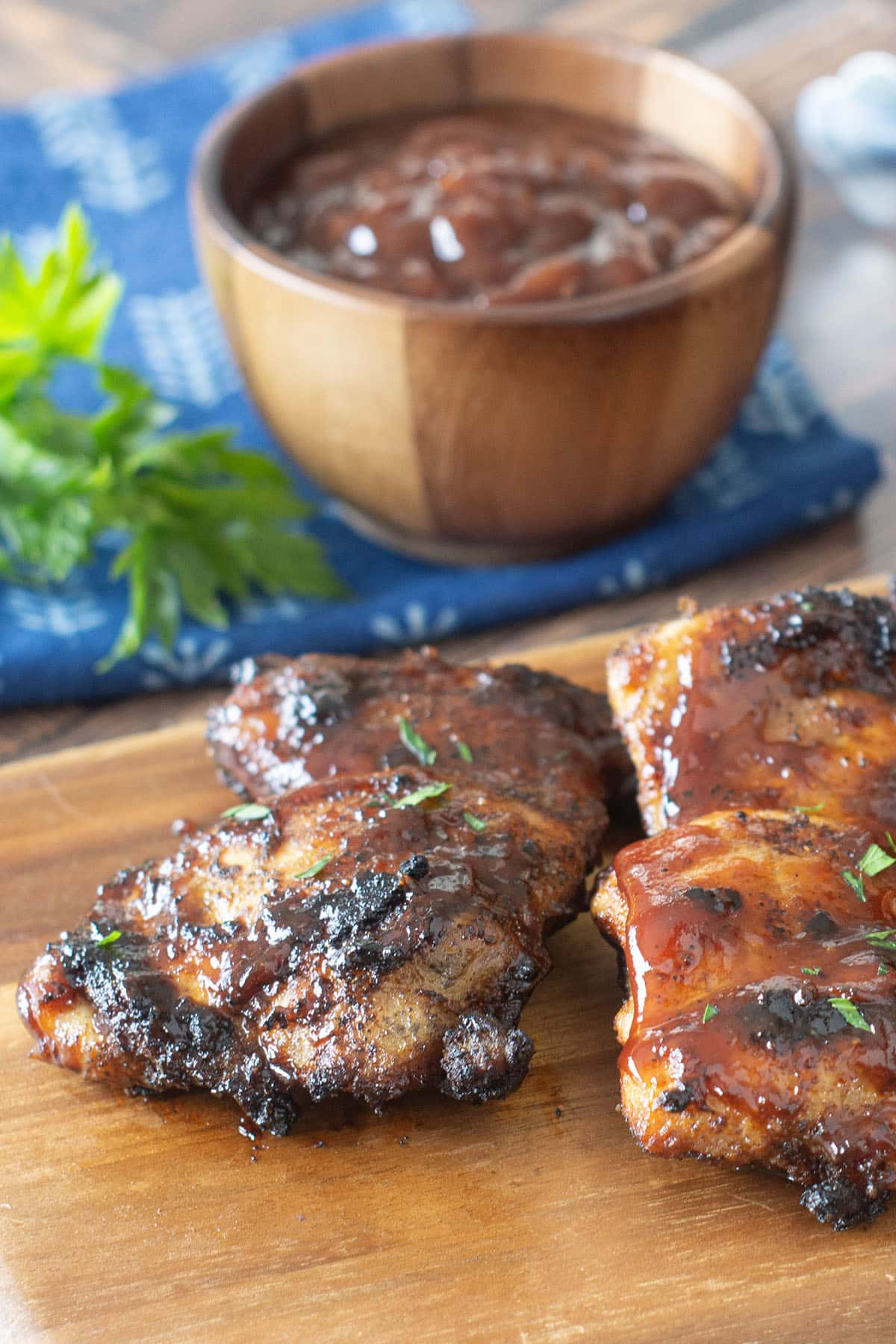 Grilled BBQ chicken thighs on a wooden cutting board.