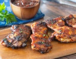 Grilled BBQ chicken thighs on a wooden cutting board.