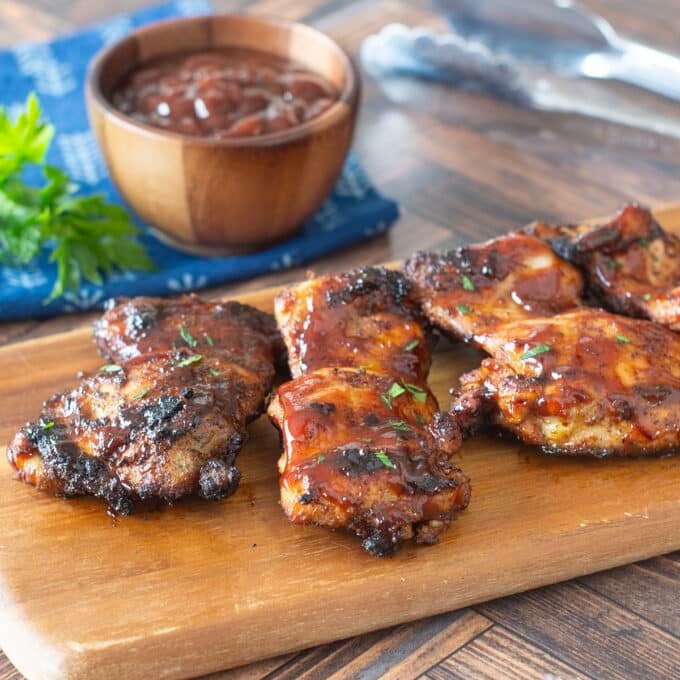 Grilled BBQ chicken thighs on a wooden cutting board.