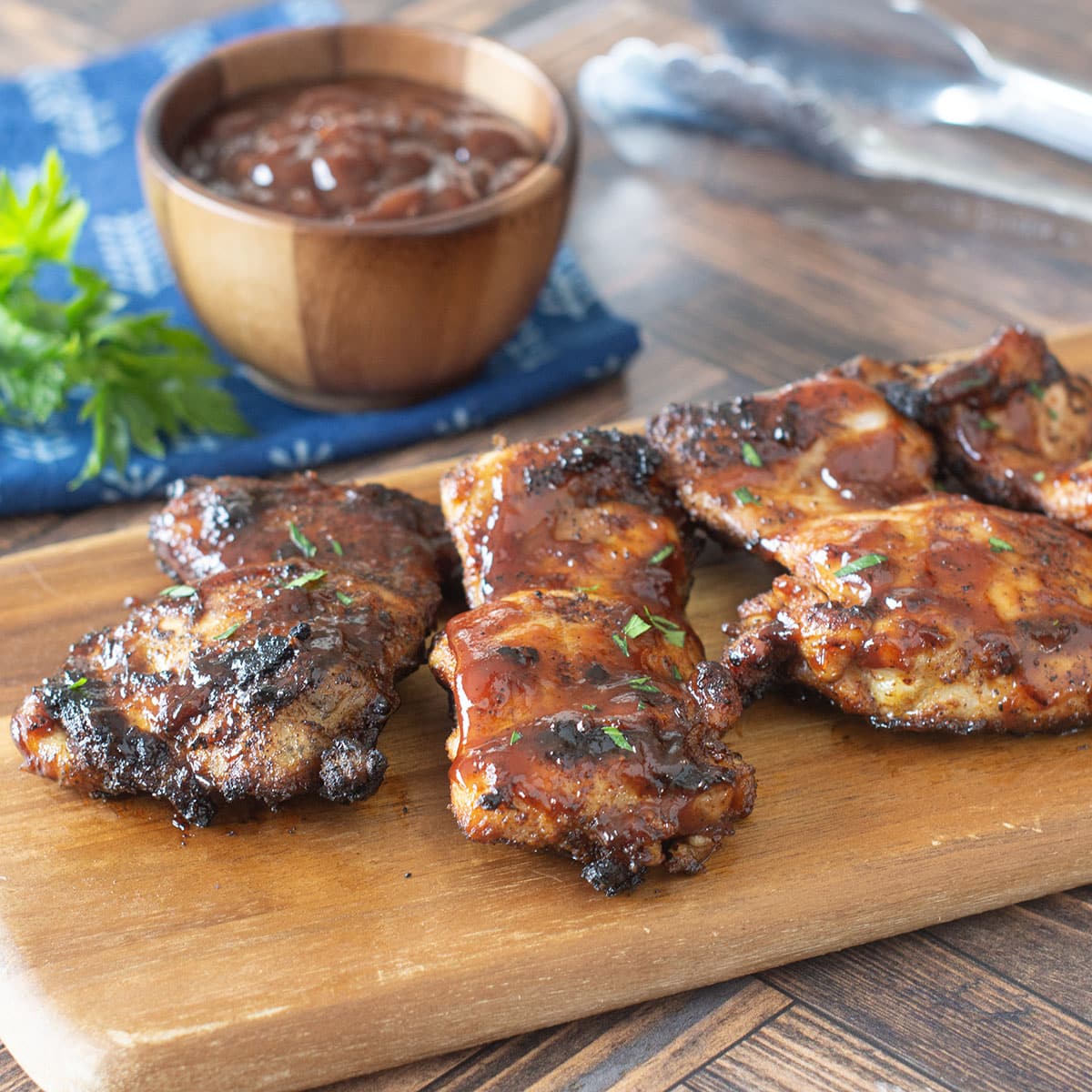 Grilled BBQ chicken thighs on a wooden cutting board.