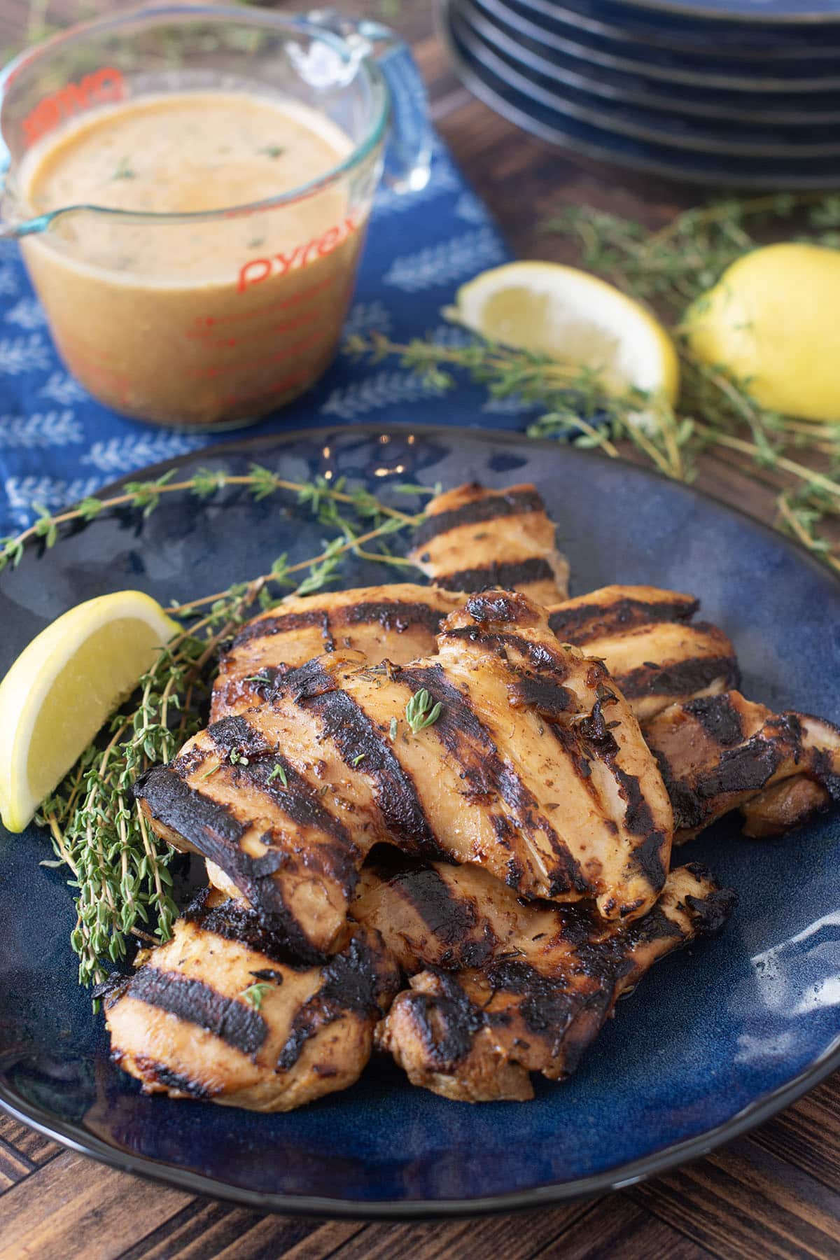 Grilled chicken thighs on blue plate with marinade in background.