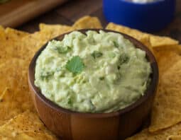 Cottage cheese guacamole in wooden bowl surrounded by tortilla chips.