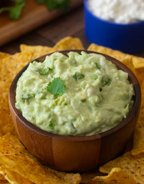 Cottage cheese guacamole in wooden bowl surrounded by tortilla chips.