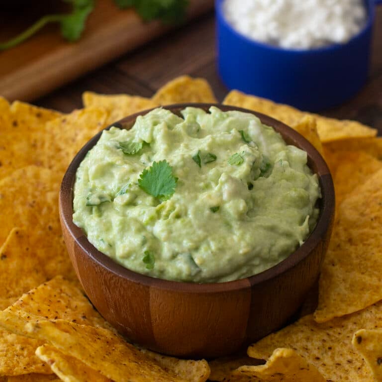 Cottage cheese guacamole in wooden bowl surrounded by tortilla chips.