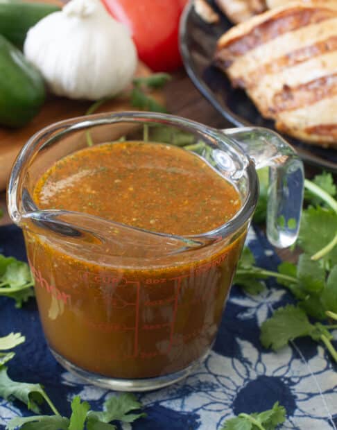 Glass measuring cup of Mexican chicken marinade surrounded by fresh ingredients like bell peppers.